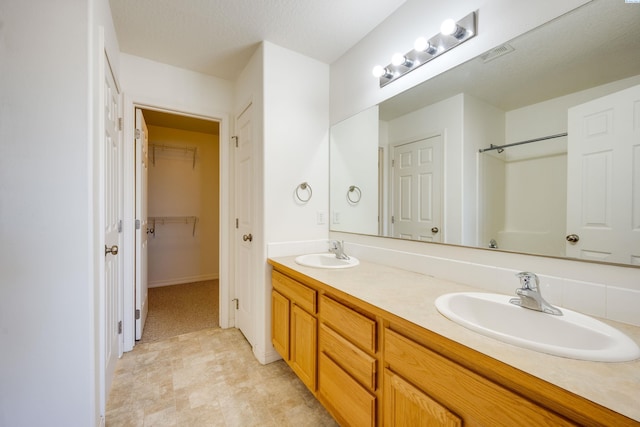 full bath with double vanity, a spacious closet, visible vents, and a sink