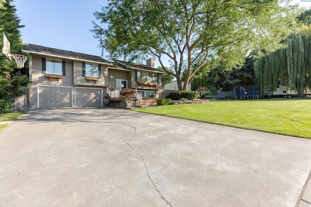 split foyer home featuring driveway, a garage, a chimney, a trampoline, and a front yard