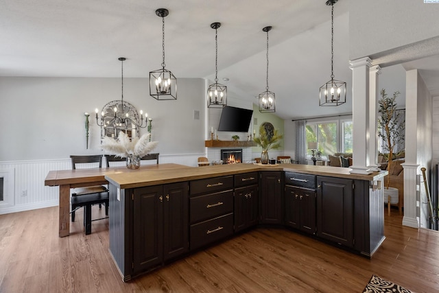 kitchen featuring wainscoting, butcher block counters, wood finished floors, vaulted ceiling, and a fireplace