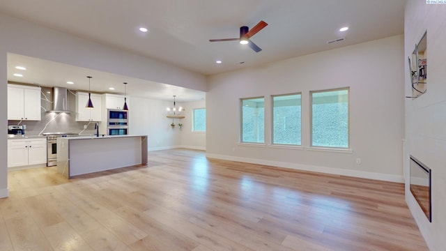 kitchen with wall chimney range hood, pendant lighting, stainless steel appliances, light hardwood / wood-style floors, and white cabinets