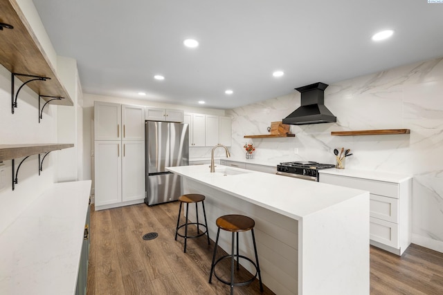 kitchen featuring sink, custom exhaust hood, white cabinetry, appliances with stainless steel finishes, and a kitchen island with sink