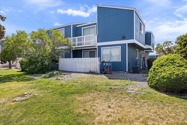 rear view of house featuring a balcony, central AC unit, and a lawn