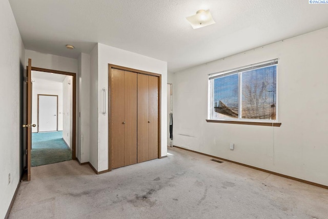 unfurnished bedroom featuring light carpet, a closet, and a textured ceiling