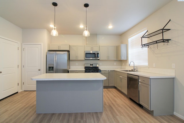 kitchen featuring appliances with stainless steel finishes, sink, a center island, gray cabinetry, and decorative light fixtures