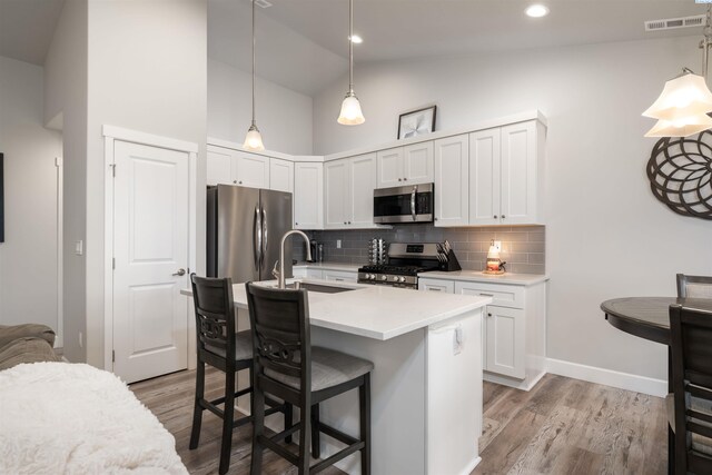 kitchen with stainless steel appliances, a sink, white cabinetry, hanging light fixtures, and light countertops