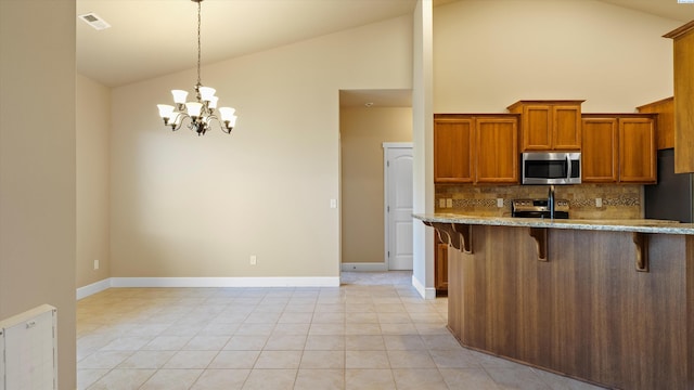 1867 S Fescue St, Kennewick, WA 99338 - kitchen featuring appliances with stainless steel finishes, a kitchen bar, backsplash, brown cabinets, and high vaulted ceiling