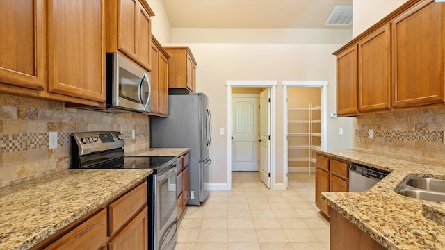 1867 S Fescue St, Kennewick, WA 99338 - kitchen featuring stainless steel appliances, brown cabinetry, backsplash, light tile patterned flooring, and light stone counters