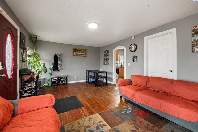 living area with arched walkways, a textured ceiling, baseboards, and wood finished floors