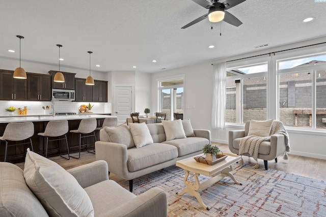 living area with light wood-type flooring, visible vents, a textured ceiling, recessed lighting, and baseboards