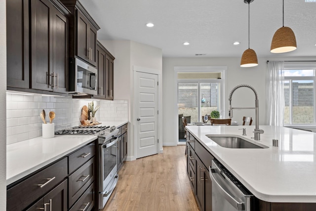 kitchen with a kitchen island with sink, a sink, stainless steel appliances, light wood-style floors, and light countertops