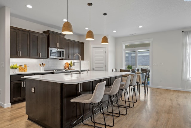 kitchen with light wood finished floors, stainless steel microwave, dark brown cabinetry, decorative backsplash, and a sink