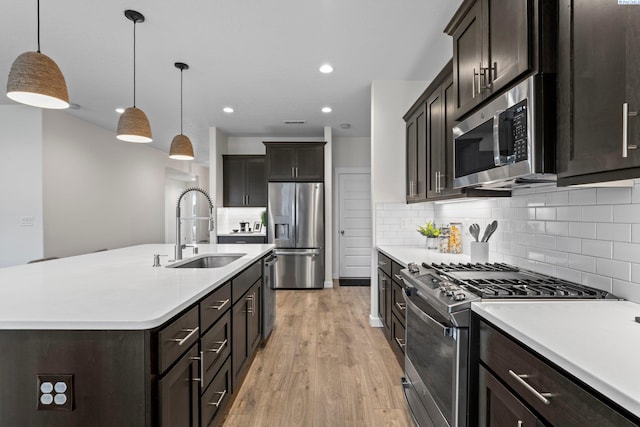 kitchen with a sink, backsplash, light wood-style floors, appliances with stainless steel finishes, and light countertops