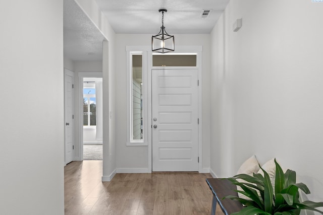 entryway featuring a textured ceiling, baseboards, visible vents, and light wood-type flooring