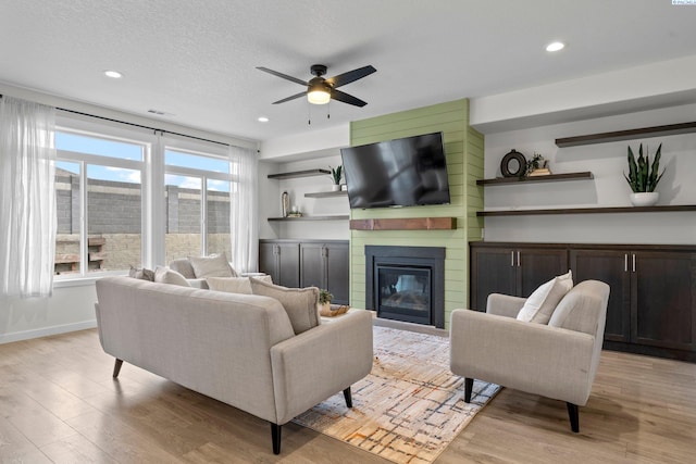 living area featuring a large fireplace, recessed lighting, a textured ceiling, and light wood-type flooring