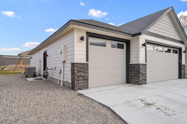 view of side of home with stone siding, roof with shingles, concrete driveway, an attached garage, and central AC unit