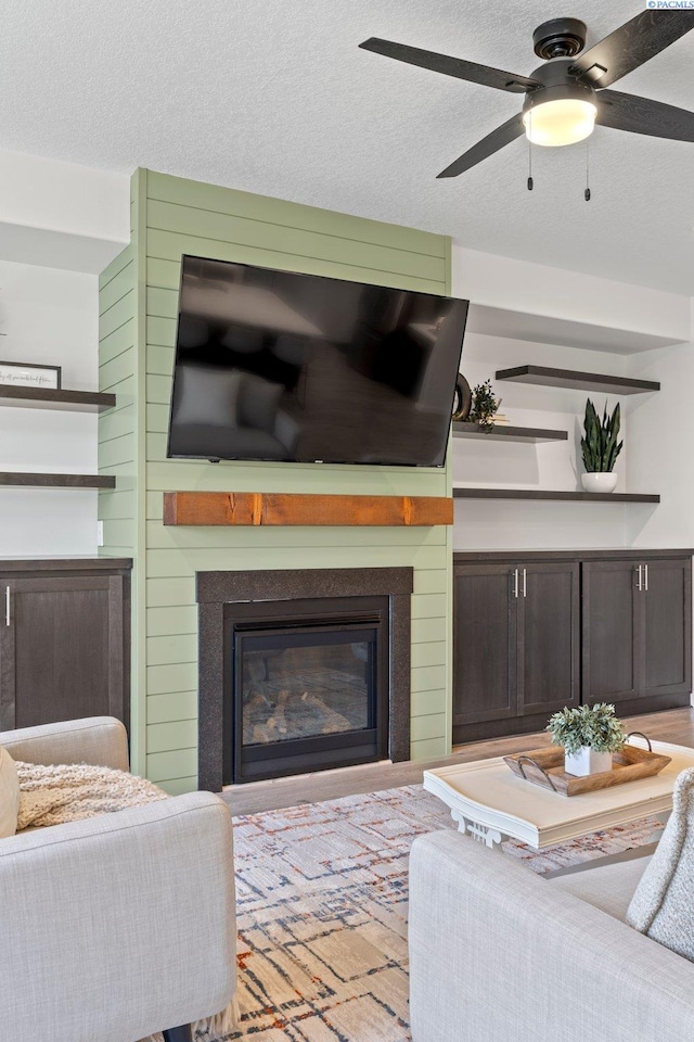 living room with a glass covered fireplace, a textured ceiling, and a ceiling fan