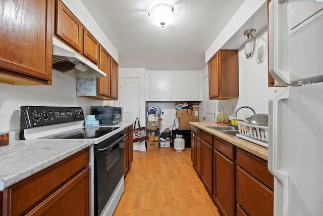 kitchen featuring brown cabinetry, electric stove, freestanding refrigerator, under cabinet range hood, and a sink