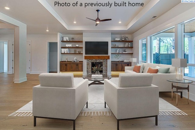 living room featuring ceiling fan, a fireplace, a raised ceiling, and light hardwood / wood-style flooring