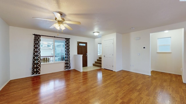 interior space featuring baseboards, stairs, light wood-type flooring, and ceiling fan