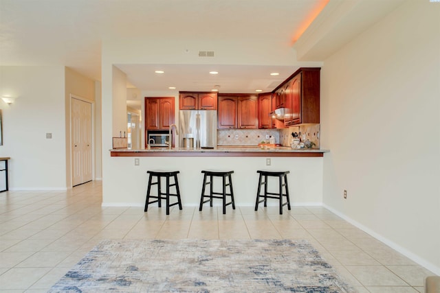 kitchen featuring stainless steel appliances, a breakfast bar, light tile patterned floors, and kitchen peninsula