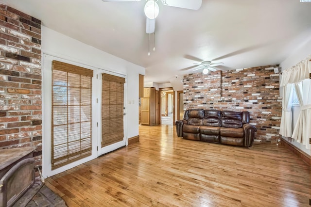 unfurnished living room featuring light hardwood / wood-style flooring, ceiling fan, and brick wall