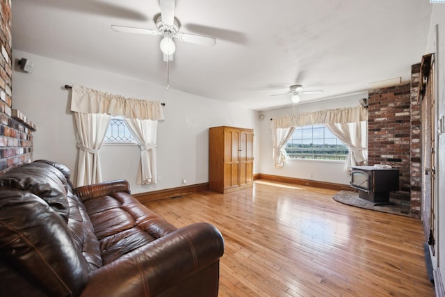 living room with a healthy amount of sunlight, a wood stove, ceiling fan, and light hardwood / wood-style flooring