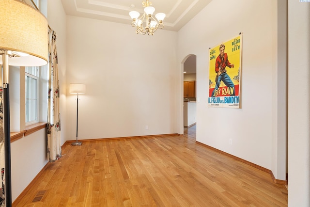 unfurnished room featuring a chandelier, light hardwood / wood-style floors, and a tray ceiling