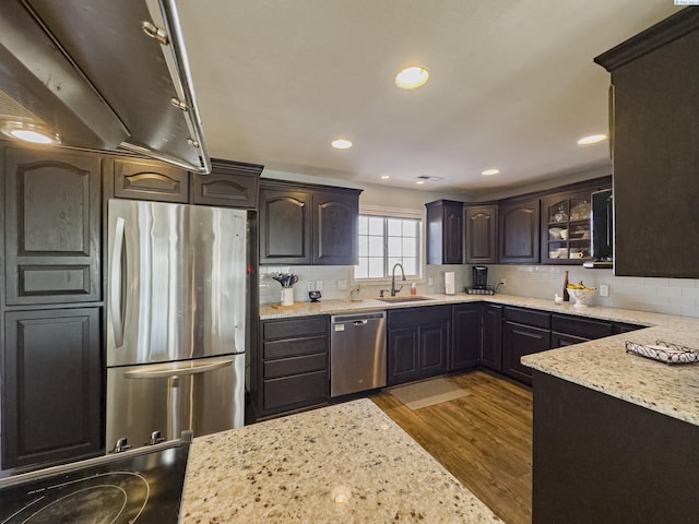 kitchen featuring sink, backsplash, stainless steel appliances, light stone counters, and light wood-type flooring