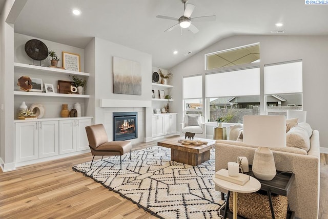 living area with built in shelves, vaulted ceiling, light wood-type flooring, ceiling fan, and a fireplace