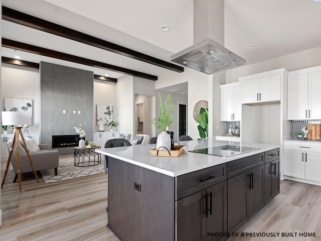 kitchen featuring white cabinetry, a center island, black electric cooktop, island exhaust hood, and a premium fireplace