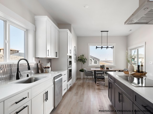 kitchen featuring sink, appliances with stainless steel finishes, white cabinets, decorative light fixtures, and wall chimney exhaust hood