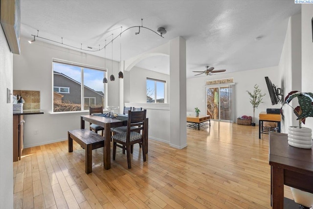 dining area with a ceiling fan, arched walkways, light wood-style floors, and baseboards