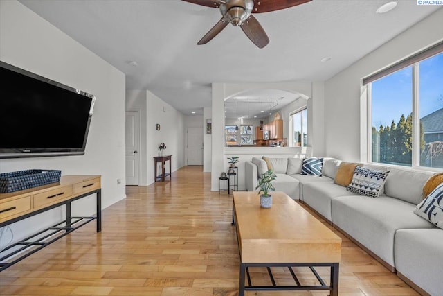 living area featuring light wood-style floors, ceiling fan, arched walkways, and baseboards