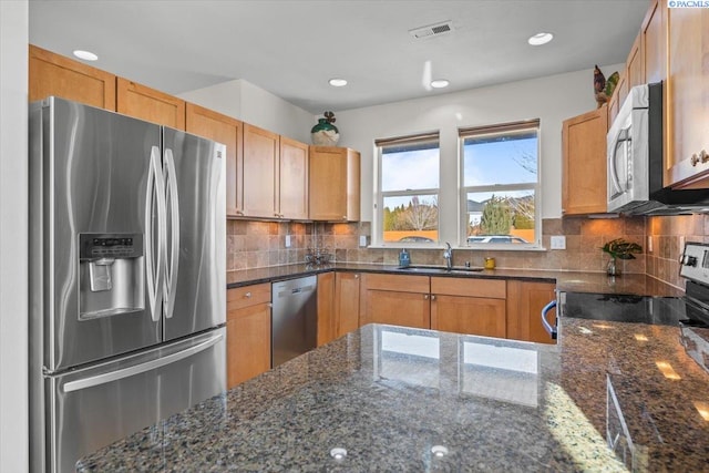 kitchen with appliances with stainless steel finishes, a sink, decorative backsplash, dark stone countertops, and recessed lighting