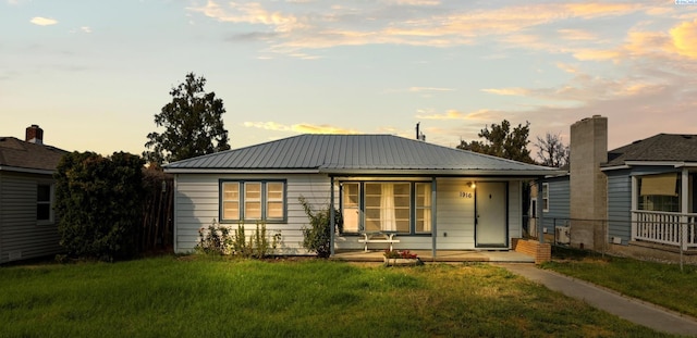 back house at dusk featuring a porch and a yard