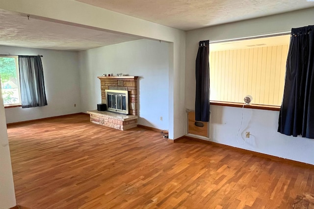 unfurnished living room with light wood finished floors, baseboards, a stone fireplace, and a textured ceiling