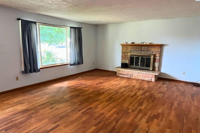 unfurnished living room with wood finished floors, a stone fireplace, baseboards, and a textured ceiling