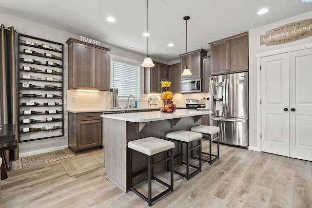 kitchen featuring pendant lighting, stainless steel appliances, dark brown cabinetry, a kitchen island, and light wood-type flooring