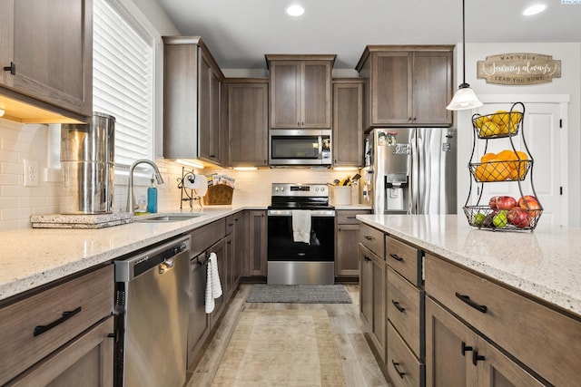 kitchen featuring sink, backsplash, stainless steel appliances, light stone countertops, and decorative light fixtures