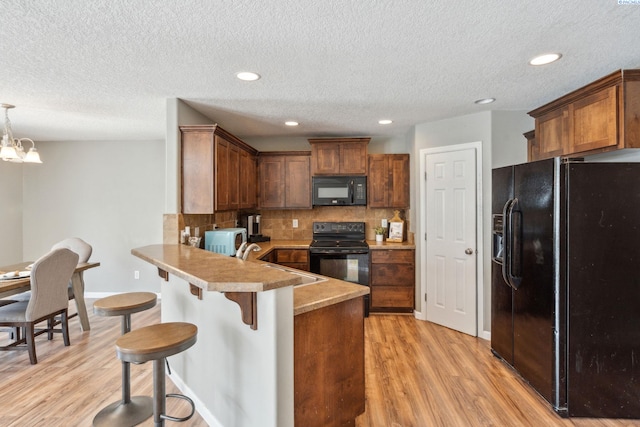 kitchen featuring a breakfast bar area, light wood-style flooring, a sink, black appliances, and a peninsula