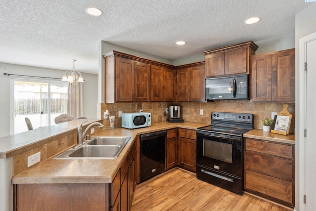 kitchen with black appliances, light wood finished floors, a sink, a notable chandelier, and a peninsula