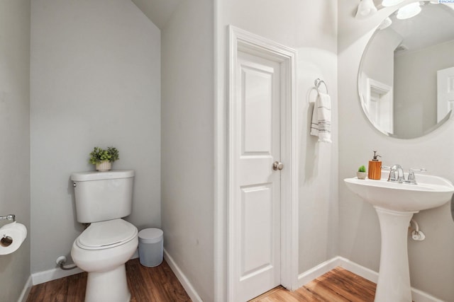 half bath featuring a sink, wood finished floors, toilet, and baseboards