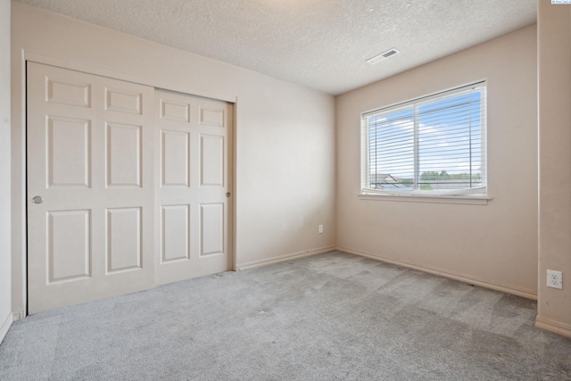 unfurnished bedroom featuring a closet, visible vents, baseboards, a textured ceiling, and carpet floors