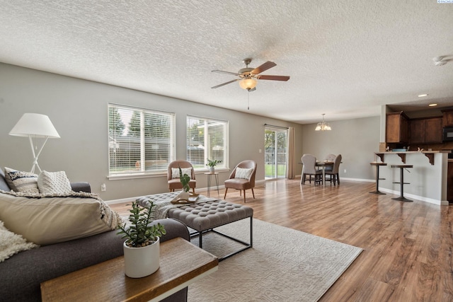 living room featuring ceiling fan with notable chandelier, a textured ceiling, wood finished floors, and plenty of natural light