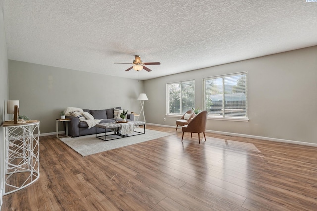 living area featuring a textured ceiling, ceiling fan, wood finished floors, and baseboards