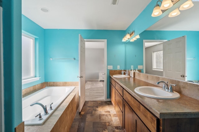 full bathroom featuring a garden tub, double vanity, a sink, and stone finish flooring