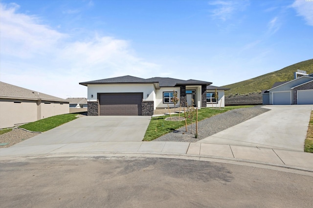 prairie-style home featuring driveway, stone siding, an attached garage, a mountain view, and stucco siding