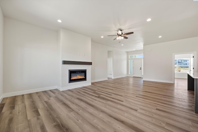 unfurnished living room with a glass covered fireplace, ceiling fan, light wood-style flooring, baseboards, and recessed lighting
