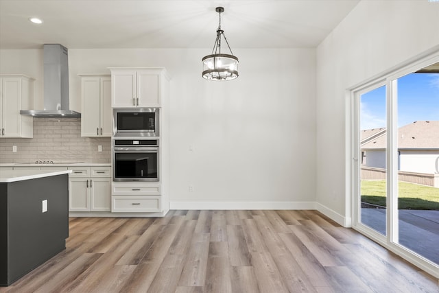 kitchen with wall chimney range hood, a wealth of natural light, appliances with stainless steel finishes, and light countertops