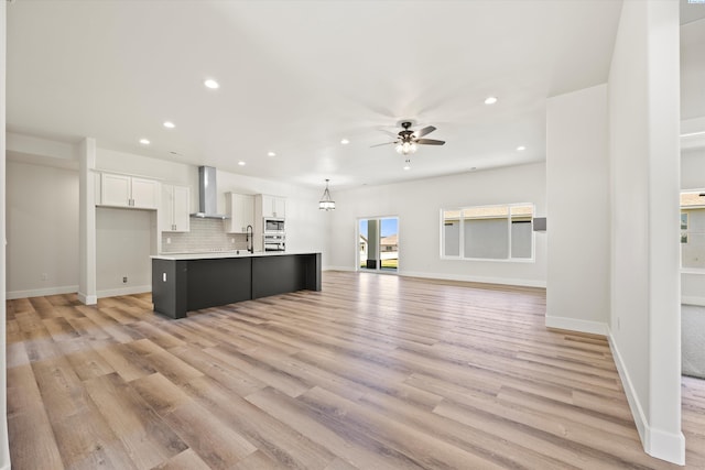 kitchen with a sink, a kitchen island with sink, wall chimney exhaust hood, appliances with stainless steel finishes, and recessed lighting